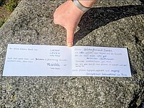 Auf dem Bild ist eine aufgeklappte Grußkarte zu sehen. Sie liegt auf einem großen Stein.