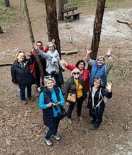 Eine Gruppe von Frauen steht zwischen Bäumen und lächelt zu der Kamera über ihren Köpfen.