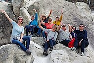 Eine Gruppe von Frauen sitzt auf einer Felsformation und winkt in die Kamera.