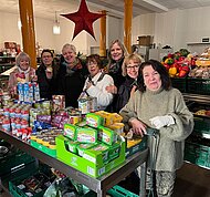 Eine Gruppe von Frauen steht hinter einem Tisch, der voller Lebensmittel ist. Alle lächeln in die Kamera.