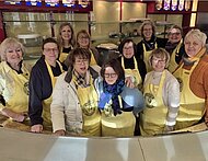 Eine Gruppe von Frauen steht hinter einem Tresen. Alle tragen gelbe Schürzen.